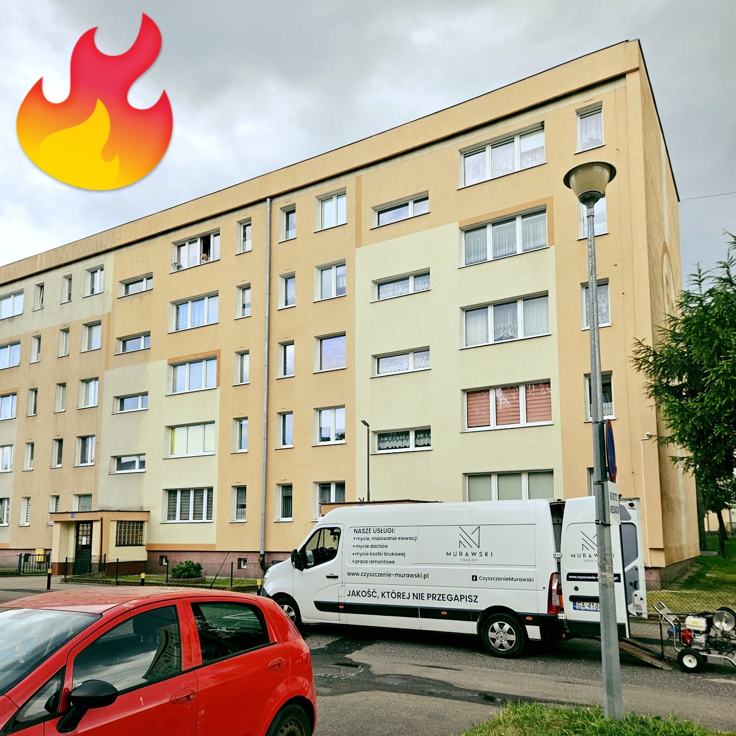 Wielopiętrowy budynek po renowacji elewacji, z zaparkowanym vanem firmy sprzątającej i myjką ciśnieniową. Widoczny fragment czerwonego samochodu.