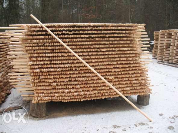 Stos ułożonych równo, okrągłych, drewnianych palików, zabezpieczony długą tyczką, na tle zimowego krajobrazu i palet