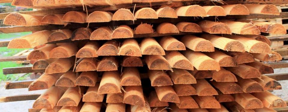 Ułożone w stos półokrągłe elementy drewniane, prawdopodobnie kantówki lub bale, widoczne słoje drewna i naturalna kolorystyka.