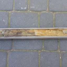 Rdzeń gruntu w metalowej rurze na tle kostki brukowej, widoczny przekrój warstw ziemi o zróżnicowanej kolorystyce.