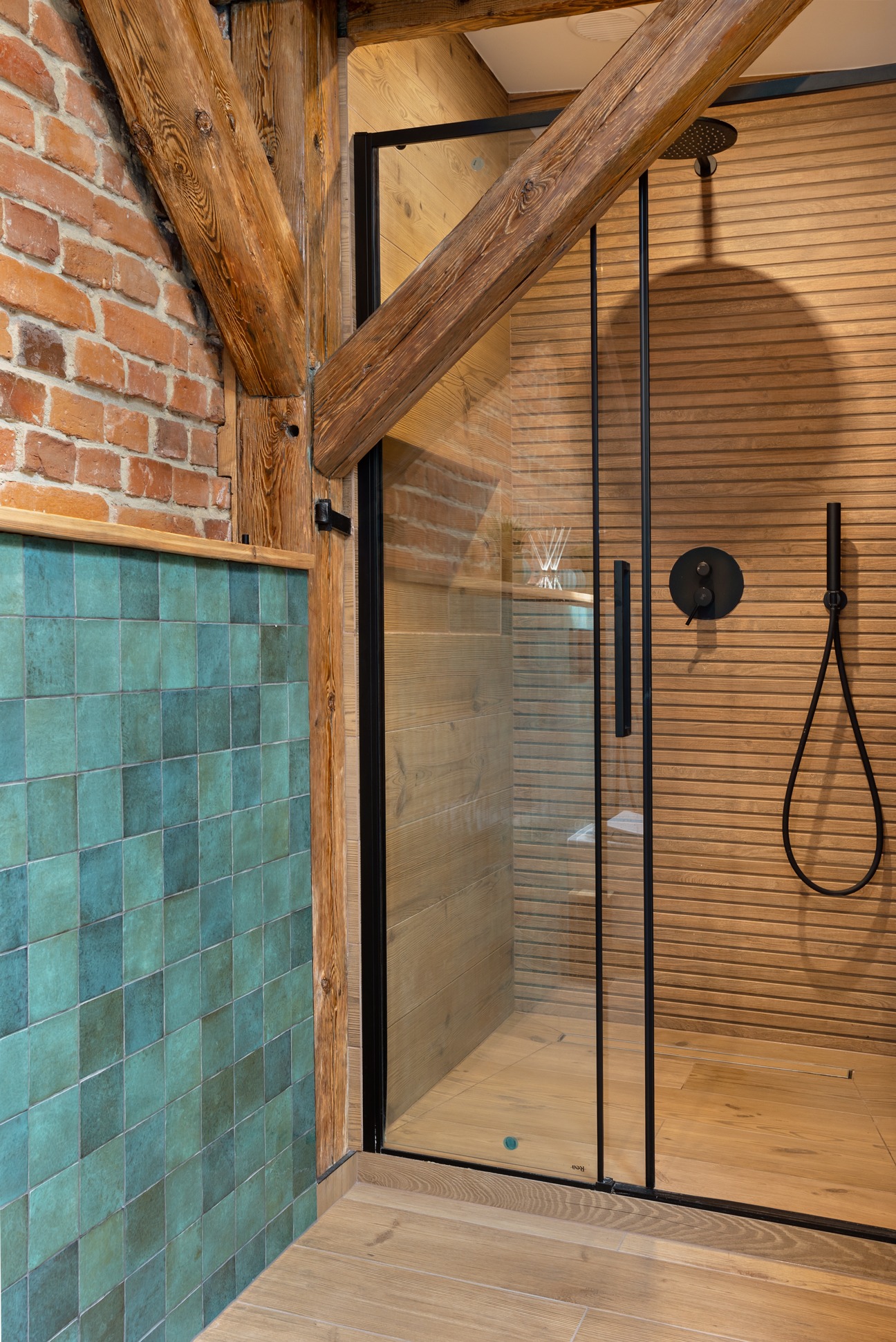 Nowoczesna kabina prysznicowa z czarnymi profilami i drewnianym wykończeniem w łazience z akcentami cegły i turkusowych płytek.