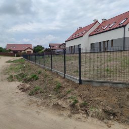 Filanowski Ogrodzenia - Nowoczesne, czarne ogrodzenie z siatki na podmurówce w Dąbrównie, widoczne domy jednorodzinne w tle, teren po budowie.