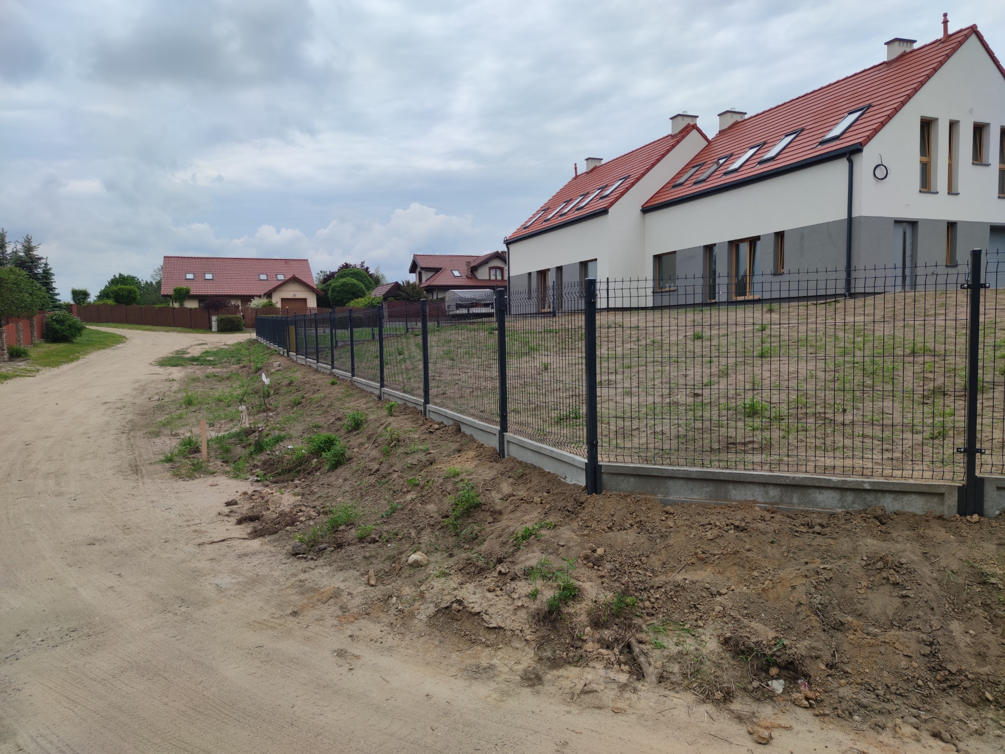 Nowoczesne, czarne ogrodzenie z siatki na podmurówce w Dąbrównie, widoczne domy jednorodzinne w tle, teren po budowie.