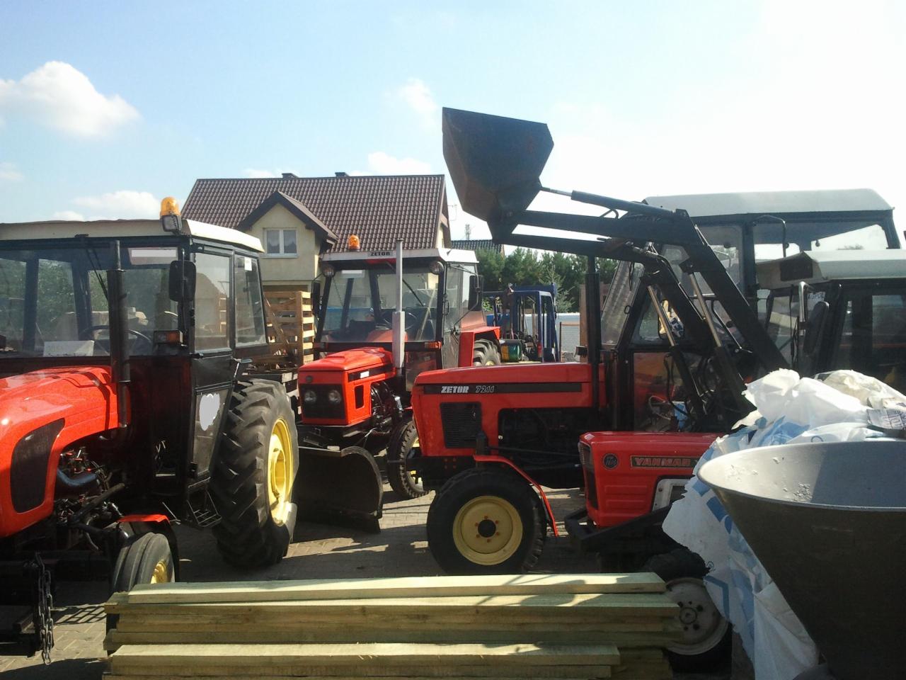 Kilka czerwonych traktorów Zetor zaparkowanych obok siebie, z widocznymi elementami konstrukcyjnymi i drewnianymi belkami na pierwszym planie.