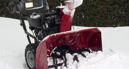 Czerwona odśnieżarka spalinowa w trakcie pracy, usuwająca świeży śnieg z powierzchni.