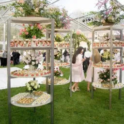 Eleganckie ekspozycje przekąsek i deserów na metalowych regałach z kwiatami, ustawione na trawniku podczas wydarzenia plenerowego w Skrzyszowie.