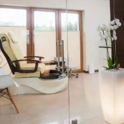 Jasny fotel do pedicure z hydromasażem, białe krzesło, sprzęt kosmetyczny i biała orchidea w podświetlanej donicy w salonie.