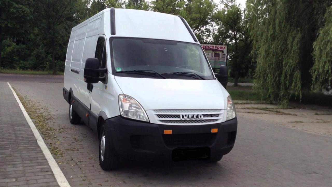 Biały samochód dostawczy marki Iveco zaparkowany na kostce brukowej, z widocznymi drzewami w tle.