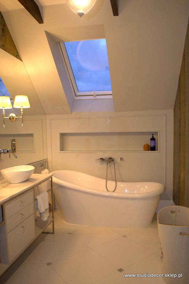 Jasna łazienka na poddaszu z wanną wolnostojącą, umywalką nablatową, oknem dachowym i wnęką w ścianie z kosmetykami.
