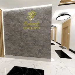 Korytarz w budynku mieszkalnym z marmurową podłogą, szarą ścianą z podświetlonym logo dewelopera i drewnianymi elementami dekoracyjnymi.