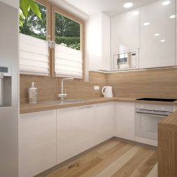 MAKAREWICZ Projekt - Jasna kuchnia w stylu skandynawskim z białymi szafkami, drewnianym blatem i podłogą, okno z żaluzjami rzymskimi, srebrna lodówka z dozownikiem wody i owocami w misce.