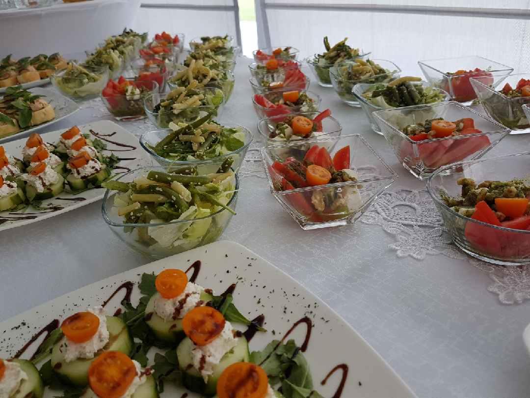 Elegancko zastawiony stół z różnorodnymi przekąskami: sałatki w szklanych miseczkach z pomidorami i zielonymi warzywami, talerze z koreczkami z ogórka, sera i pomidorków koktajlowych, całość...