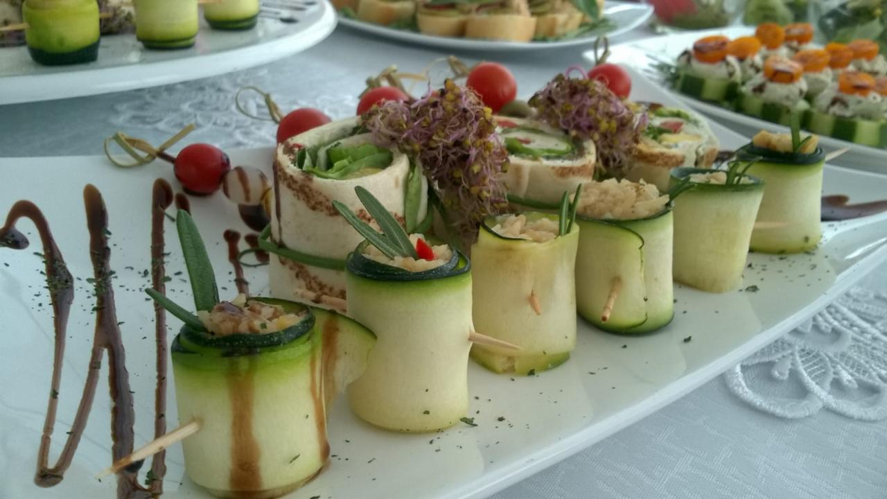 Elegancko podane przystawki: roladki z tortilli z zielonymi pędami, cukiniowe ruloniki z farszem, dekorowane ziołami i balsamicznym sosem na białym talerzu z koronkową serwetą w tle.