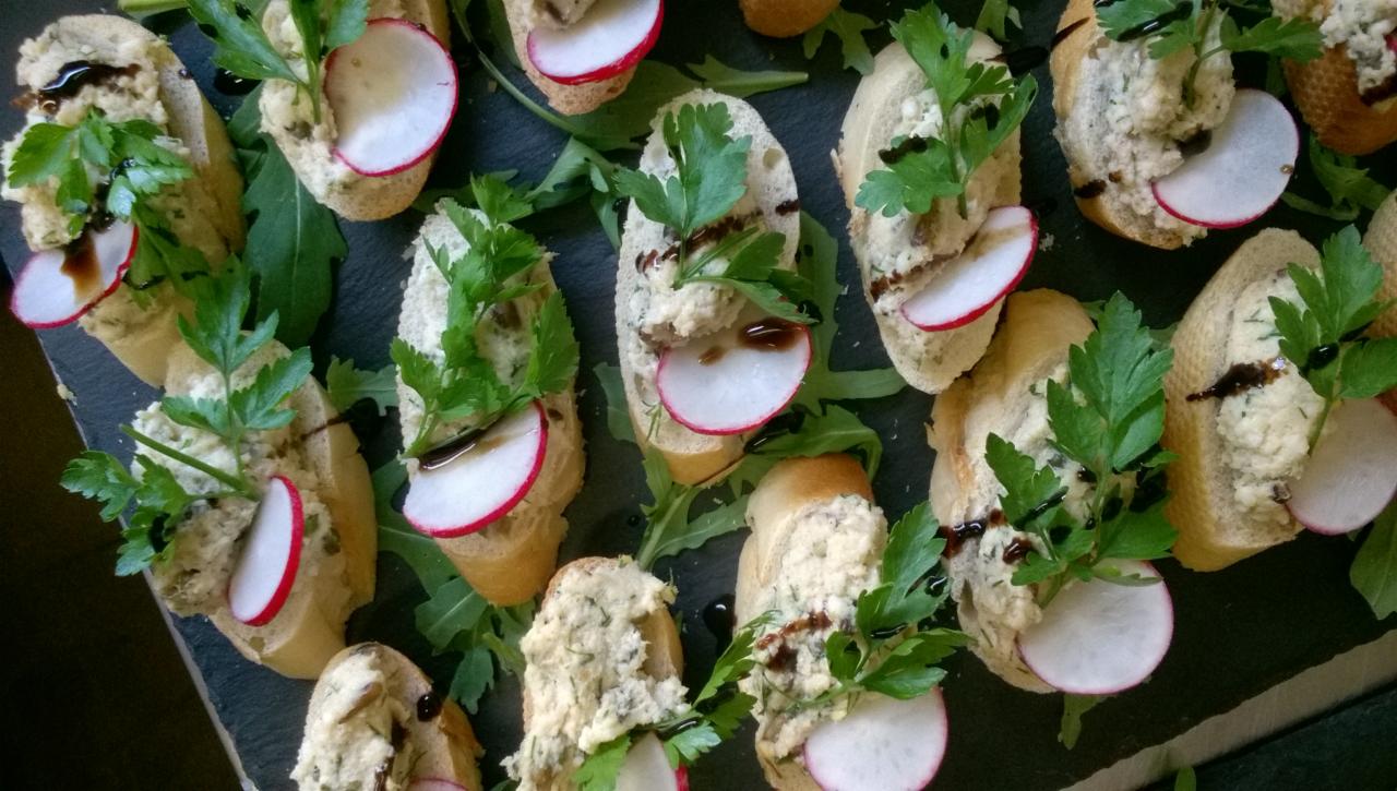 Apetyczne kanapeczki z pastą, rzodkiewką i świeżą pietruszką, polane balsamicznym sosem, ułożone na ciemnym kamiennym talerzu z rukolą.