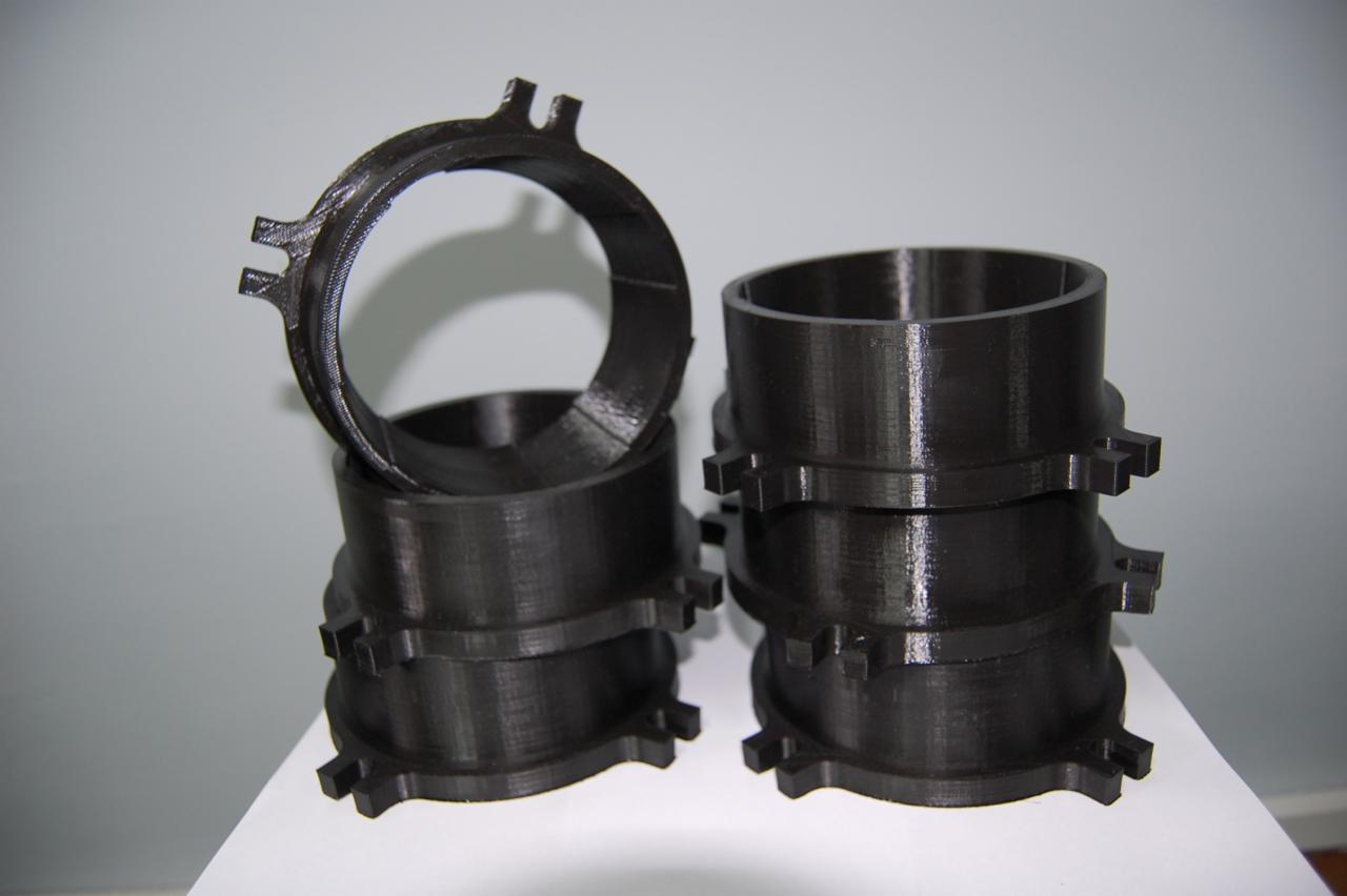 Ciemne, wydrukowane w 3D pierścienie z wypustkami, ułożone w dwie nierówne sterty na białym tle, widoczna struktura warstw druku.