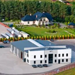 Widok z lotu ptaka na bazę firmy transportowej z budynkami biurowymi, warsztatem i zaparkowanymi cysternami oraz ciężarówkami.