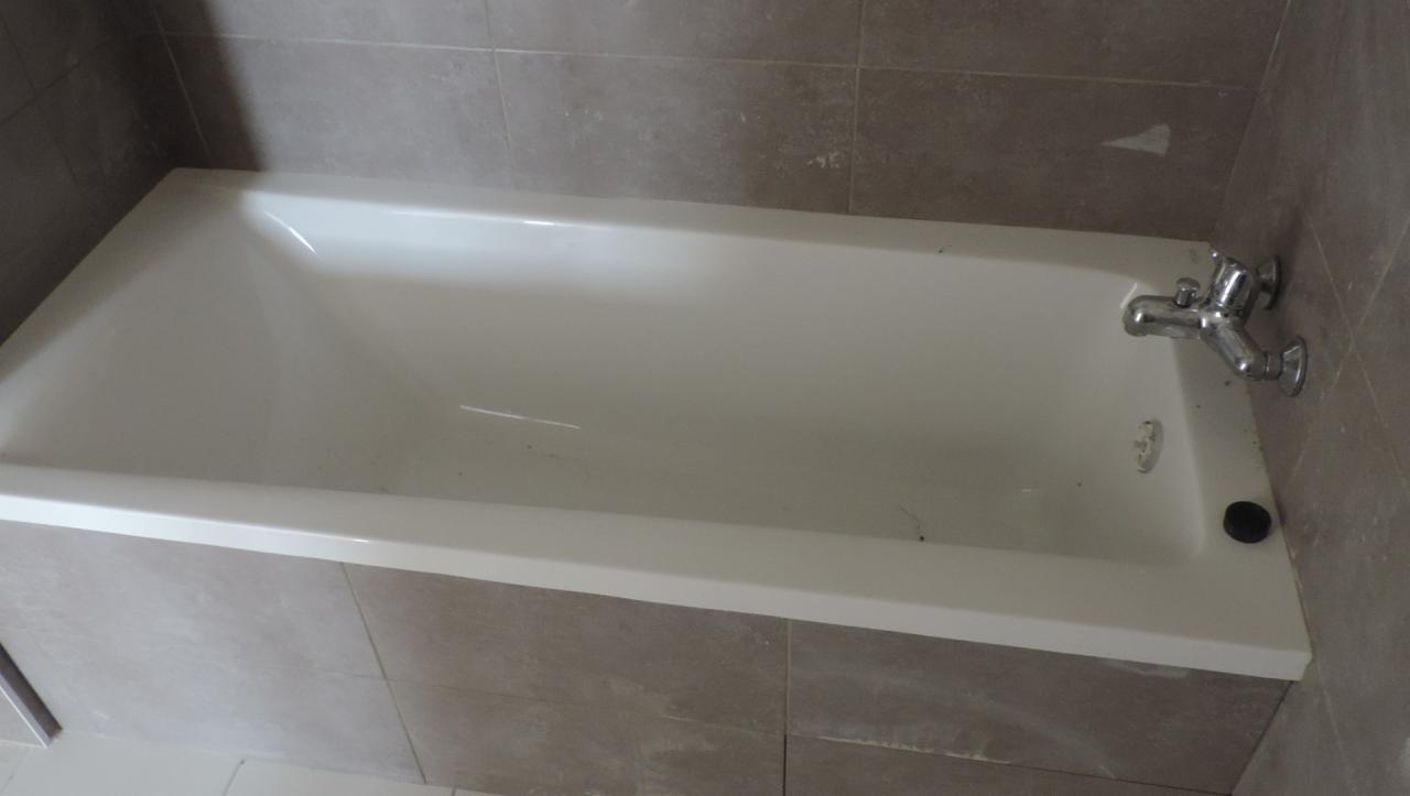 Biała wanna po remoncie, obłożona szarymi płytkami, z chromowaną baterią i czarnym korkiem.