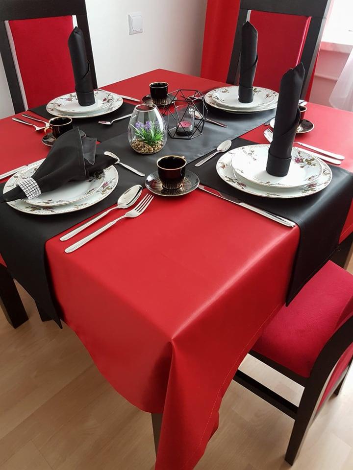 Uroczysty stół nakryty czerwonym obrusem, czarny bieżnik, elegancka zastawa z kwiatowym motywem, czarne serwetki ze srebrną obrączką, czarne filiżanki i geometryczny świecznik z tealightem, mała...