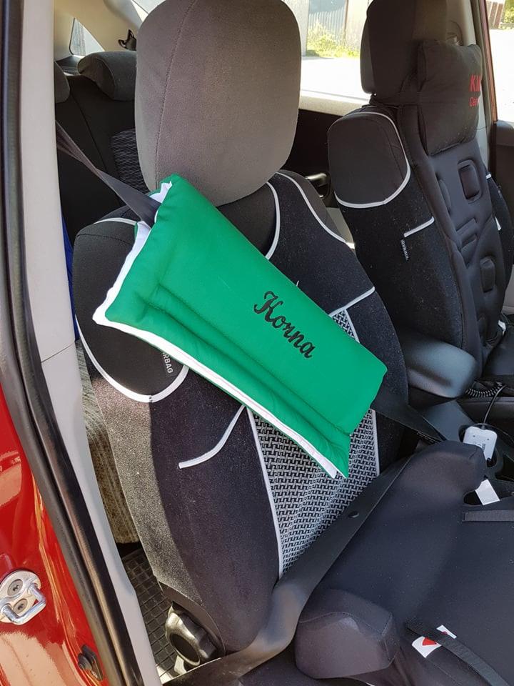 Zielona, pikowana nakładka na pas bezpieczeństwa z białym obszyciem i czarnym haftem imienia 'Korna' wewnątrz czerwonego samochodu.