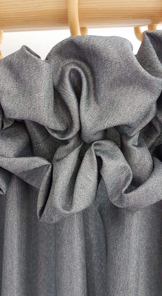 Szara zasłona z marszczeniem na drewnianym karniszu, widoczne detale faktury materiału i fałdy.