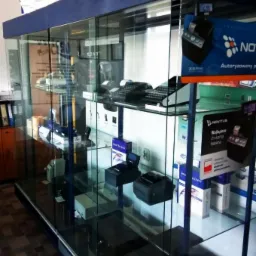 Szklana witryna sklepowa z kasami fiskalnymi, drukarkami fiskalnymi i akcesoriami biurowymi, w tle ściana i szafka.