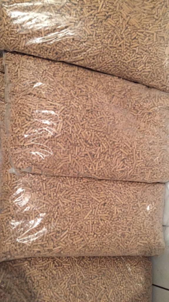 Stos worków wypełnionych jasnymi, drewnianymi pelletami, widoczne z bliska, z lekkim odblaskiem światła na plastikowych workach.