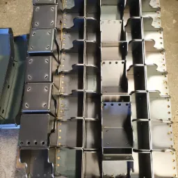 Partie spawanych, metalowych elementów konstrukcyjnych o nieregularnym kształcie, ułożonych na palecie, widoczne ślady spawania punktowego.