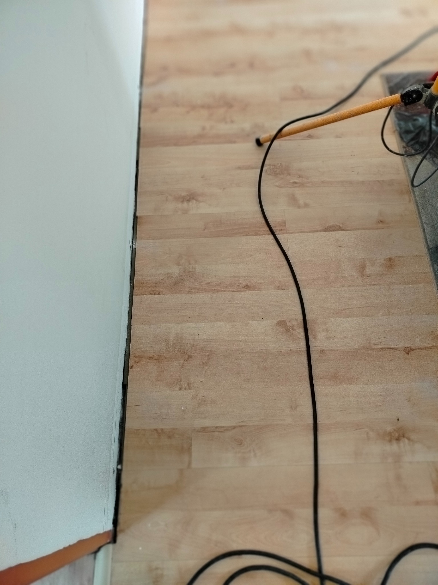 Fragment pokoju po ułożeniu jasnych paneli podłogowych, widoczna ściana z listwą przypodłogową i kabel od urządzenia na panelach. Ujęcie z góry.