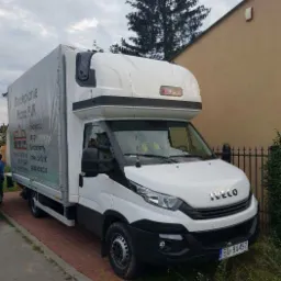 Biały samochód dostawczy Iveco z plandeką z nadrukiem reklamowym firmy świadczącej usługi docieplania pianą PUR, zaparkowany na chodniku przed budynkiem.
