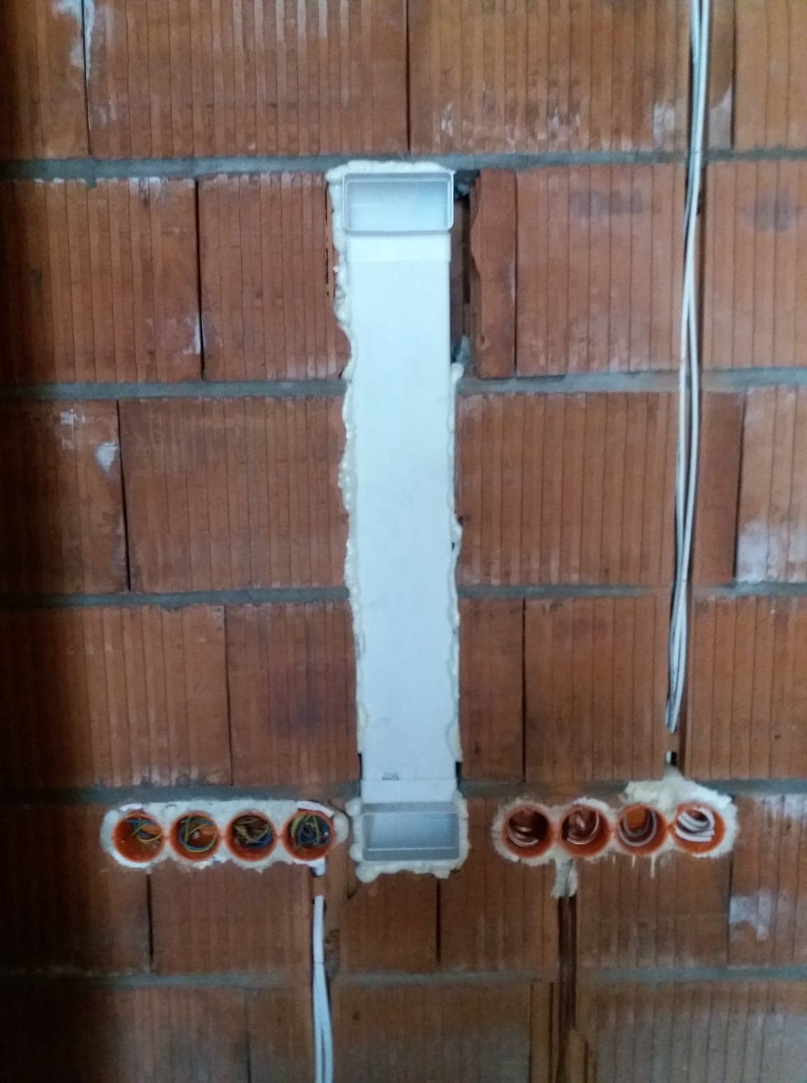 Montaż przewodów w ścianie z cegły dziurawki i puszek instalacyjnych, zabezpieczonych pianką montażową w Kłomnicach.
