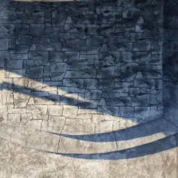 Szara ściana z betonu architektonicznego imitującego kamień, z widocznymi śladami formowania i padającym cieniem, tworząca element dekoracyjny.
