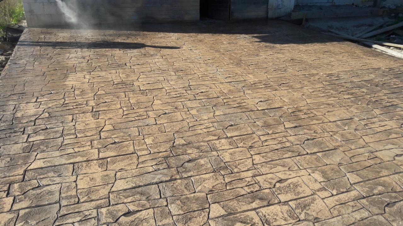 Świeżo ułożona, brązowa nawierzchnia z betonu stemplowanego imitująca kamienną posadzkę, czyszczona strumieniem wody pod ciśnieniem.