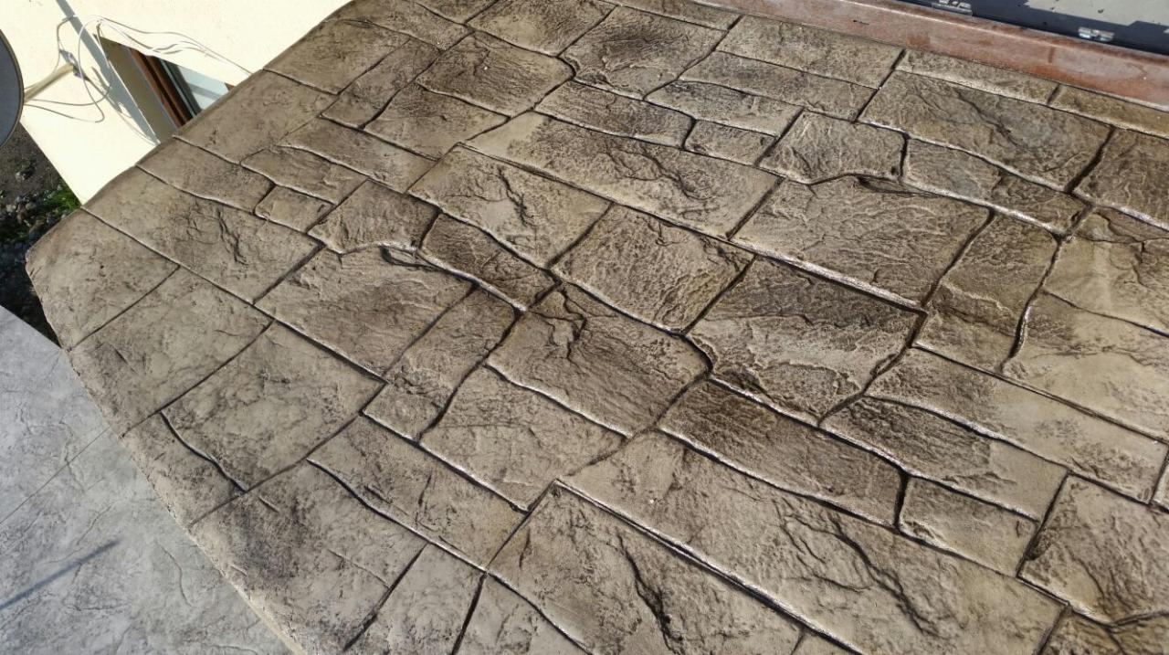 Szara powierzchnia z betonu stemplowanego imitująca kamienną posadzkę, widok z góry, z delikatnym gradientem oświetlenia.