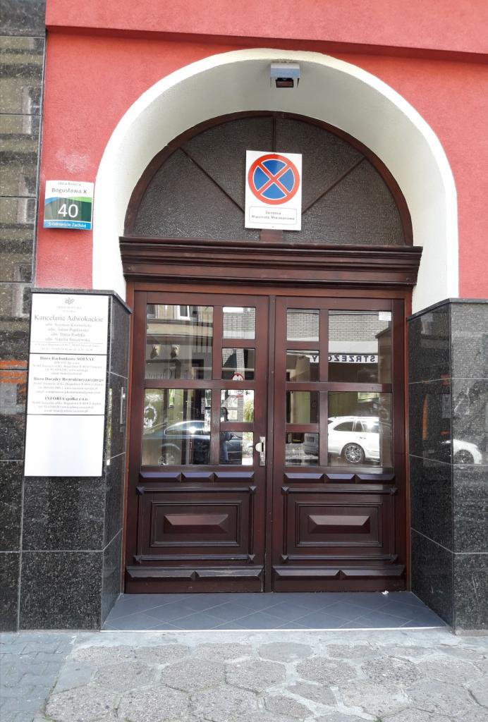 Wejście do Kancelarii Adwokackiej: drewniane dwuskrzydłowe drzwi z szybami, nad nimi znak zakazu parkowania, tabliczka z adresem Bogusława X 40 i szyld z informacjami o kancelarii.