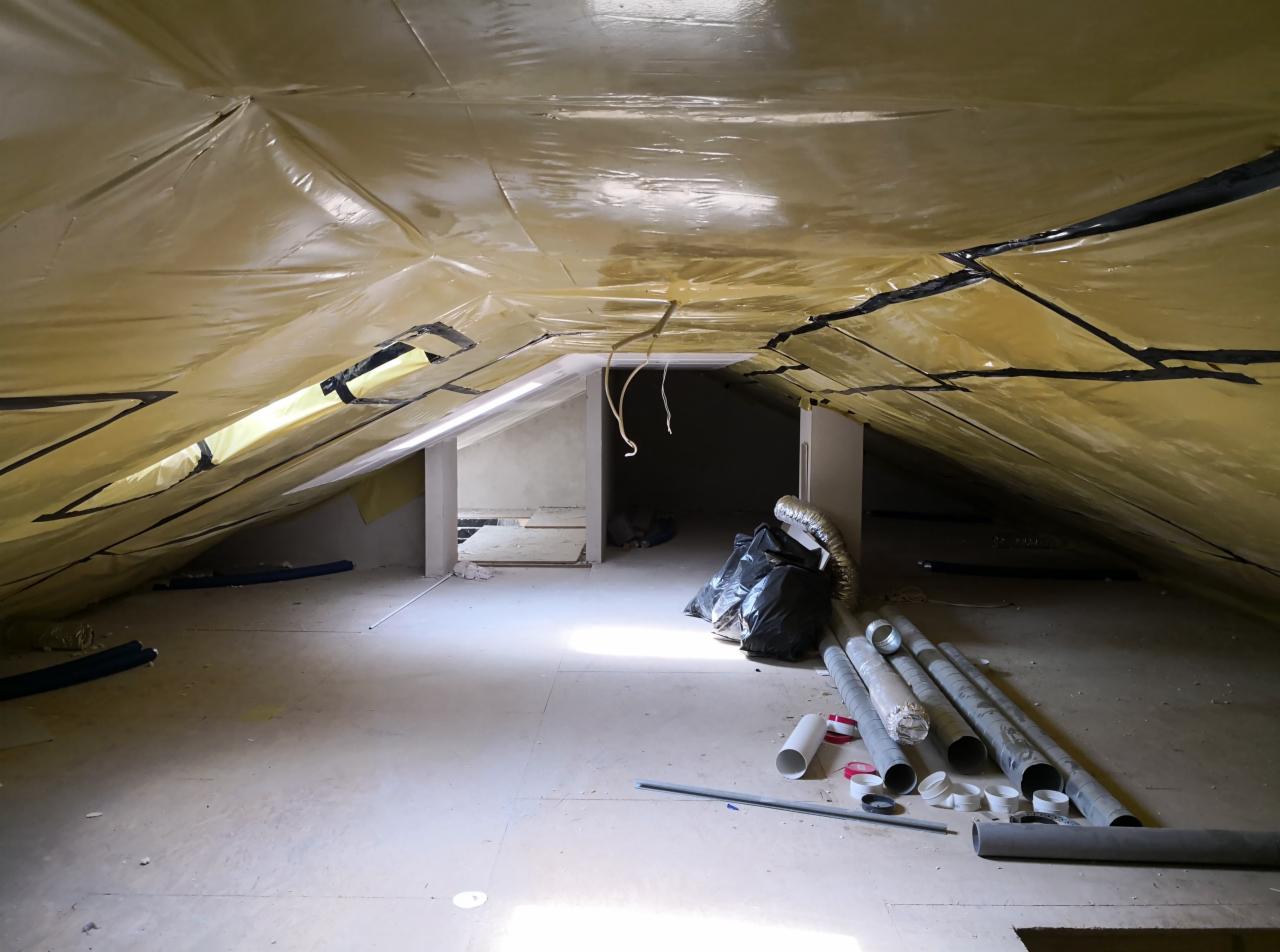 Poddasze w trakcie prac: folia paroizolacyjna na skośnym suficie, widoczne rury wentylacyjne, ściany działowe w tle.