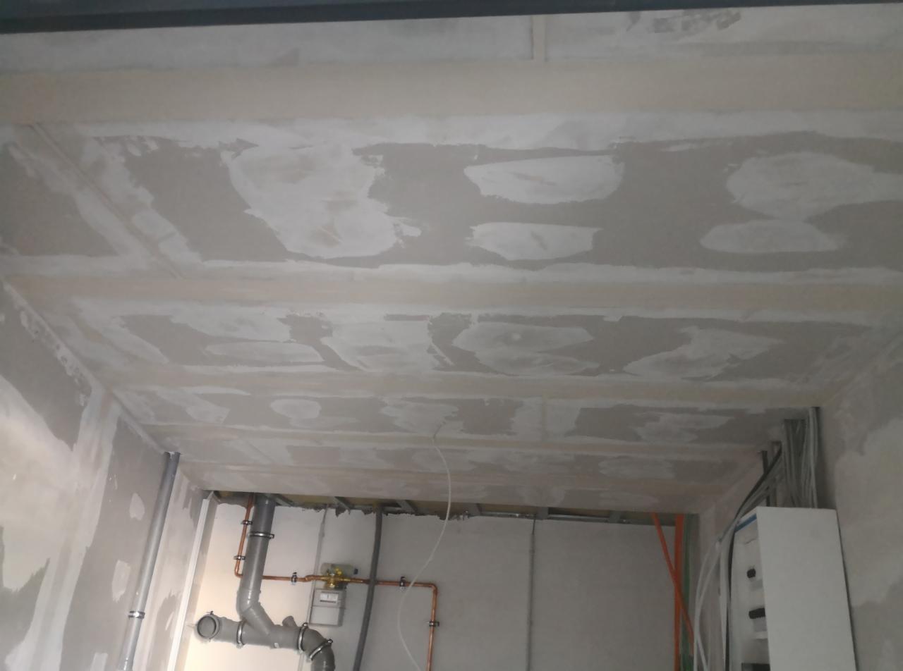 Sufit w trakcie szpachlowania, widoczne łączenia płyt i instalacja wodna w tle.