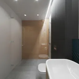 Nowoczesna łazienka z kabiną prysznicową ze szklaną ścianą, drewnianymi panelami na ścianie prysznica, białą wanną wolnostojącą i szarą podłogą z płytek.