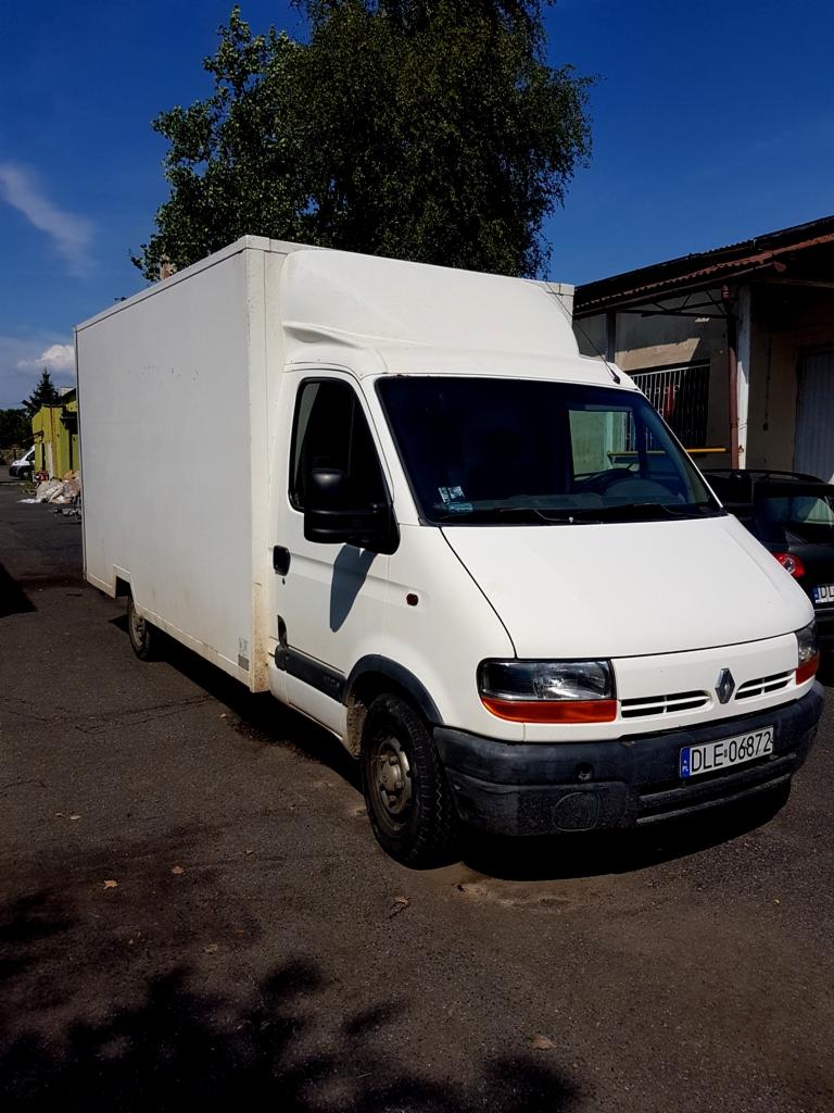 Biały samochód dostawczy Renault Master z zabudową kontenerową zaparkowany na asfalcie, widoczny numer rejestracyjny DLE-06872, obok budynek magazynowy i zaparkowany samochód osobowy, słoneczny dzień.