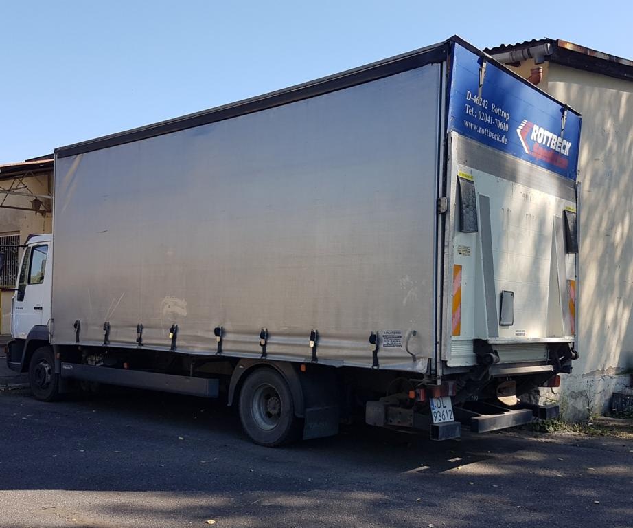 Ciężarówka z plandeką zaparkowana na ulicy, widoczny tył pojazdu z numerem rejestracyjnym i logo firmy Rottbeck na niebieskim tle.