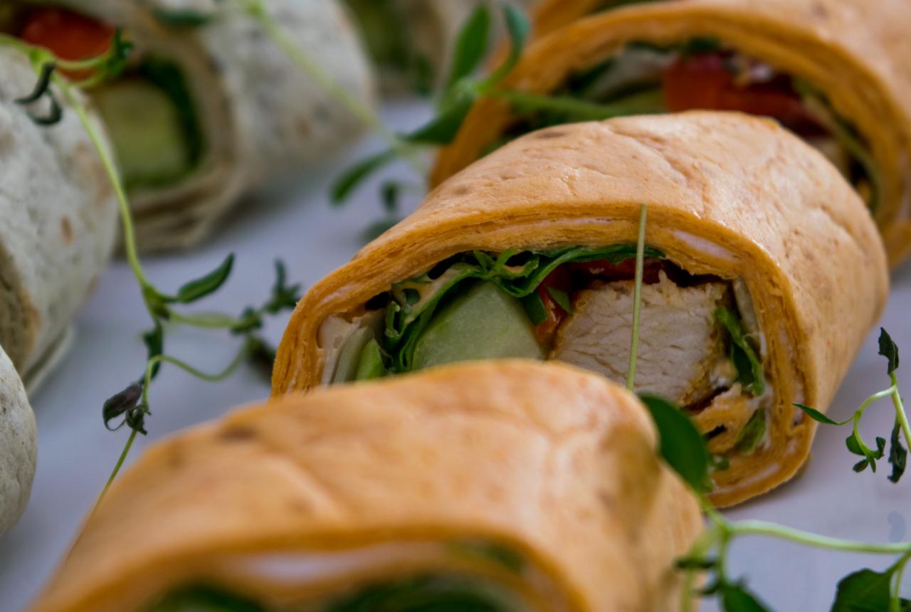 Krojone tortille z kurczakiem, sałatą, ogórkiem i pomidorem, udekorowane świeżym tymiankiem, na białym talerzu.