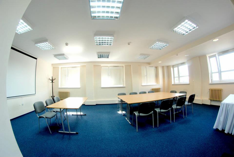 Sala konferencyjna z dwoma stołami i krzesłami, rzutnikiem i niebieską wykładziną.