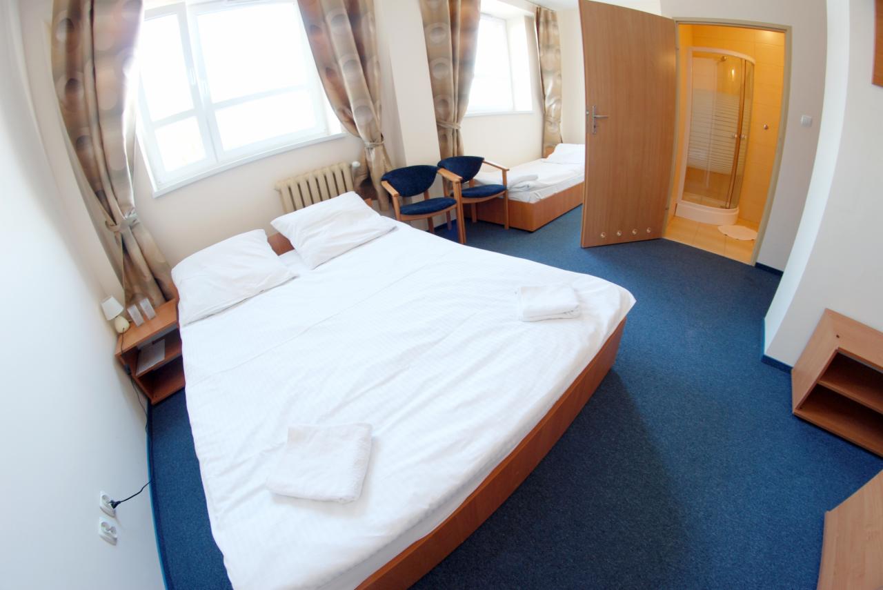 Pokój hotelowy z dwoma łóżkami, niebieską wykładziną i otwartą łazienką z kabiną prysznicową, widziany z szerokiego kąta.