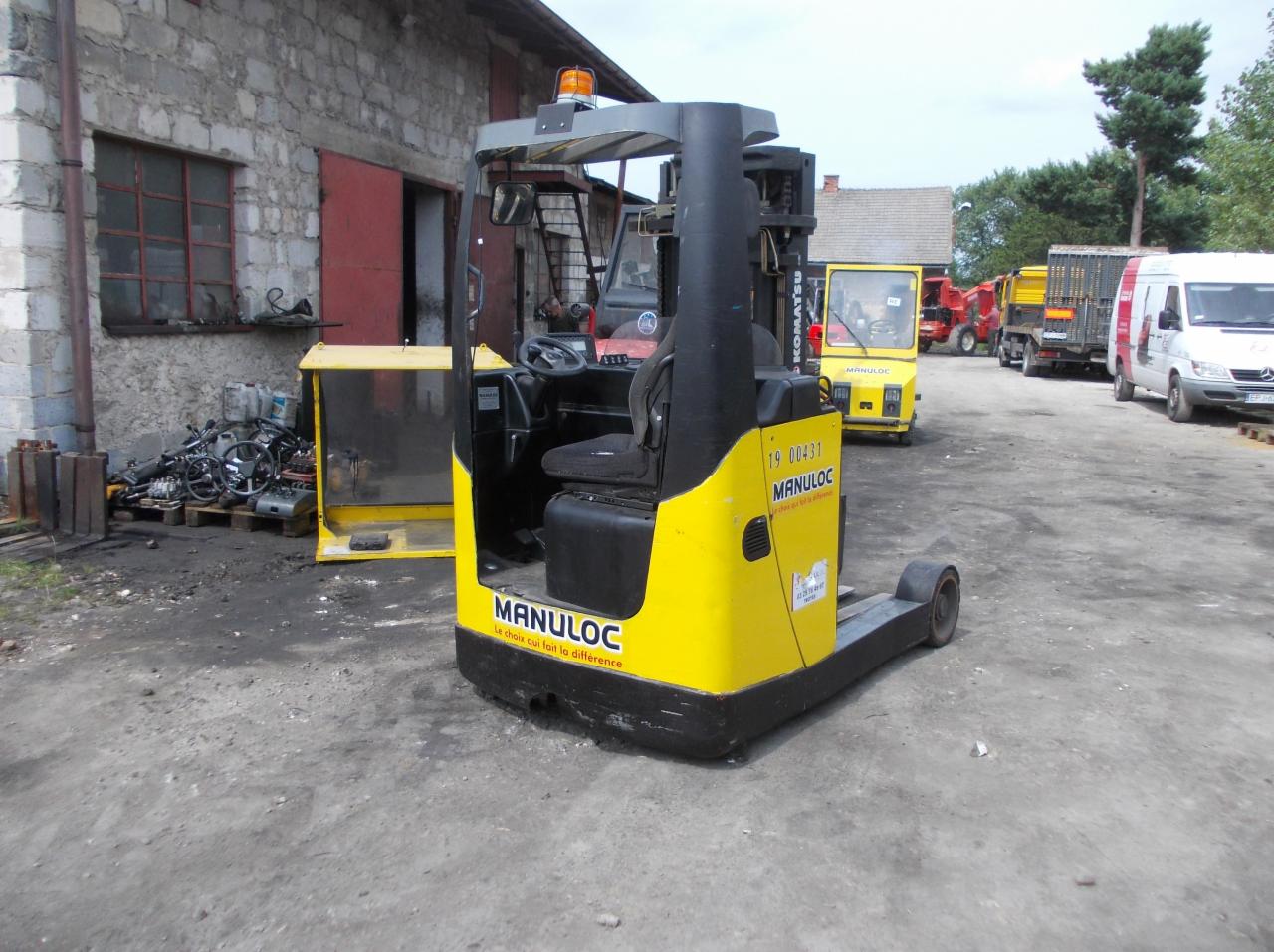 Żółto-czarny wózek widłowy z kabiną Manuloc na zewnątrz, z widocznymi innymi pojazdami i budynkiem w tle.