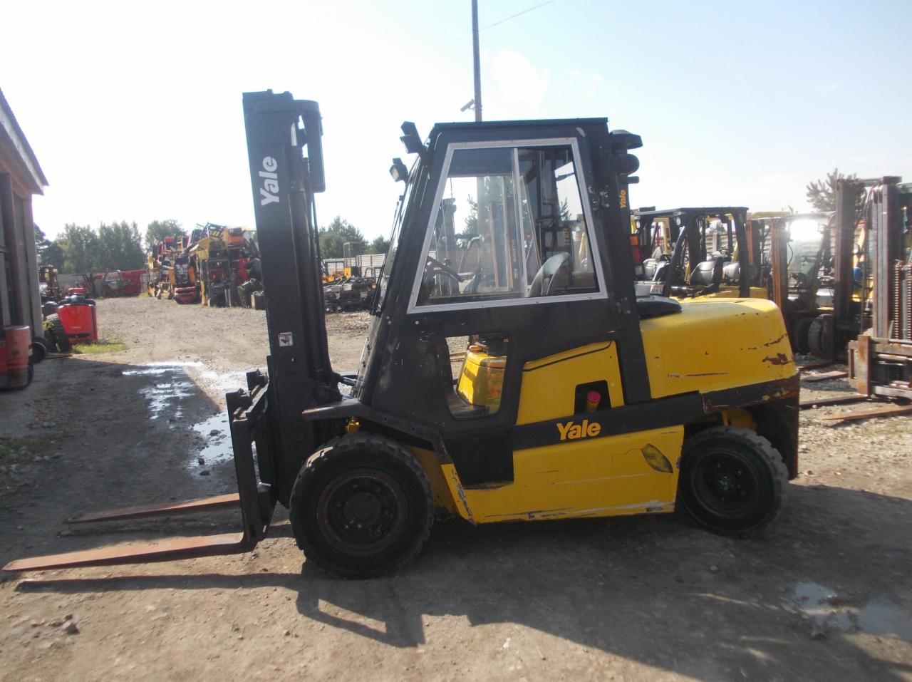 Używany, żółty wózek widłowy marki Yale na placu z innymi maszynami w tle.