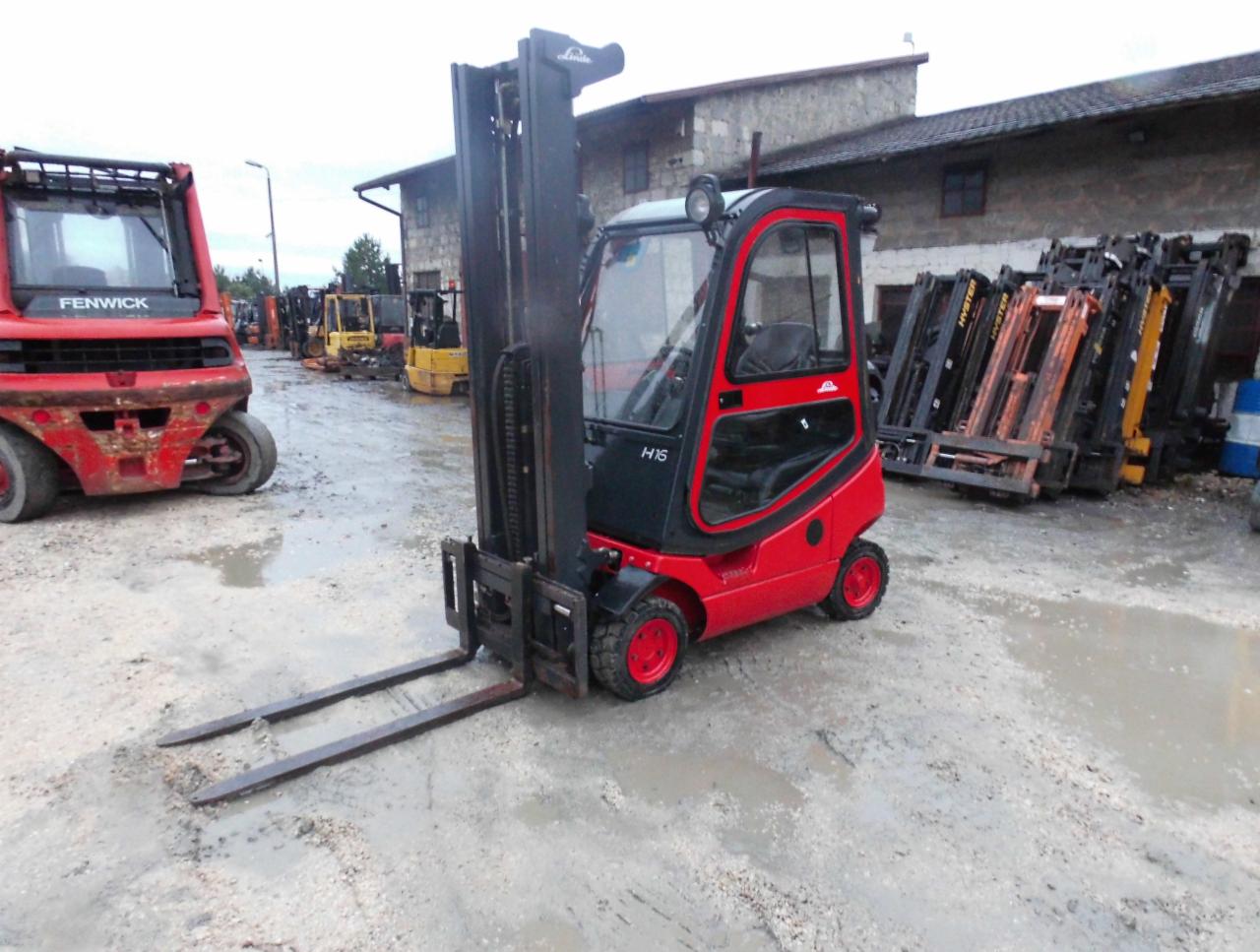 Czerwono-czarny wózek widłowy Linde H16 na placu z innymi wózkami widłowymi w tle, mokra nawierzchnia.