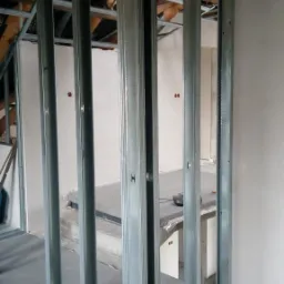 Stelaż z metalowych profili, prawdopodobnie pod ściankę działową z płyt kartonowo-gipsowych, widoczny na tle surowego wnętrza w trakcie remontu.