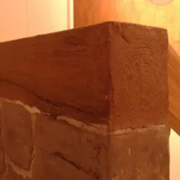 Fragment ściany z efektem dekoracyjnym imitującym starą cegłę i drewnianą belkę, obok fragment balustrady schodowej z drewna.