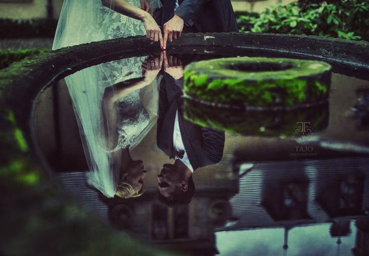 Para młoda dotyka palcami powierzchni wody w kamiennej fontannie, odbicie twarzy zakochanych w wodzie, logo TaJo photography.