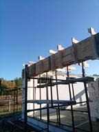 Szare bloczki fundamentowe z drewnianym szalunkiem pod wylewkę, wsparte na metalowej konstrukcji, na tle błękitnego nieba w słoneczny dzień.