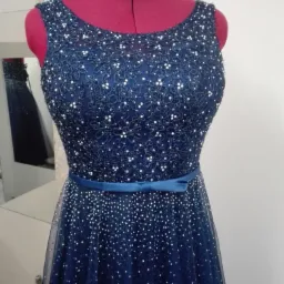 Granatowa suknia wieczorowa z koronkową górą i tiulowym dołem, zdobiona drobnymi, białymi koralikami, prezentowana na czerwonym manekinie krawieckim.